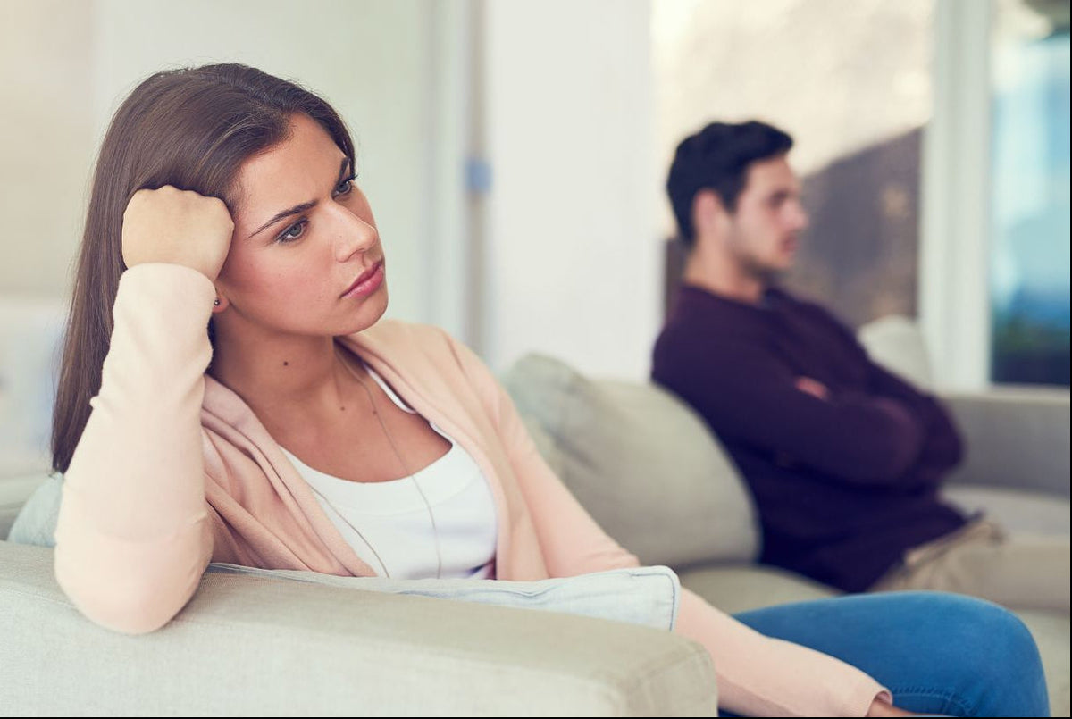A woman sits on a light gray sofa in a living room, looking sad and contemplative. Conflict resolution needed