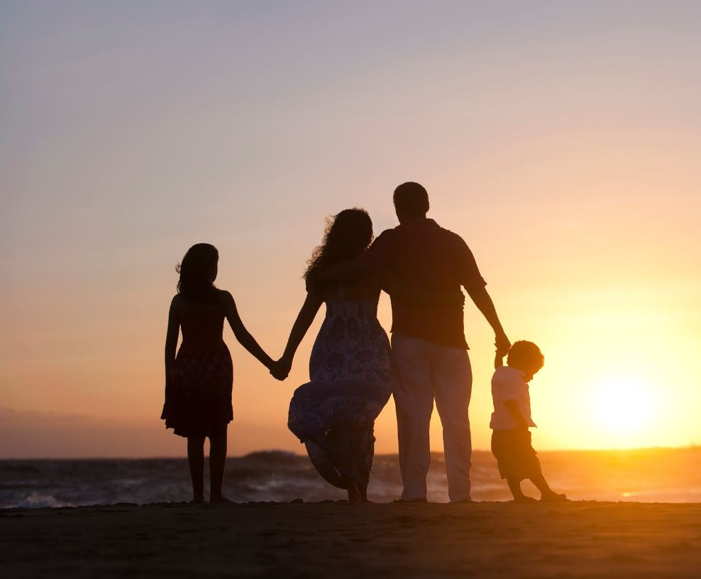 Silhouetted happy family of four walking hand in hand along a beach at sunset